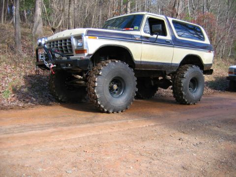 1992 Ford Mustang - A lifted 1978 Ford Bronco with oversized tires and a winch is parked on a dirt road near trees.