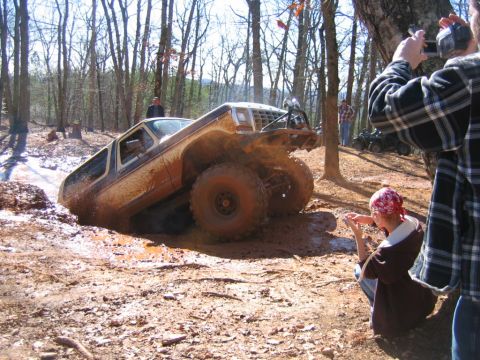 1992 Ford Mustang - A heavily modified off-road truck is stuck deep in mud while onlookers film the scene.