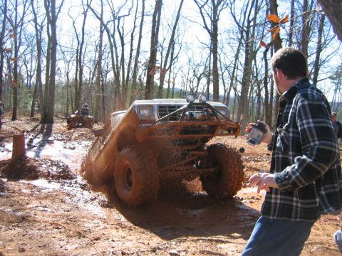 1992 Ford Mustang - Off-road vehicle struggling through a muddy obstacle course in a wooded area.