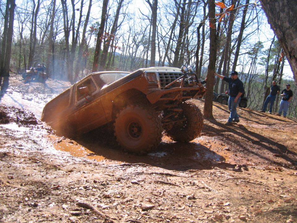 Muddy off-road truck climbing out of a ditch with people watching