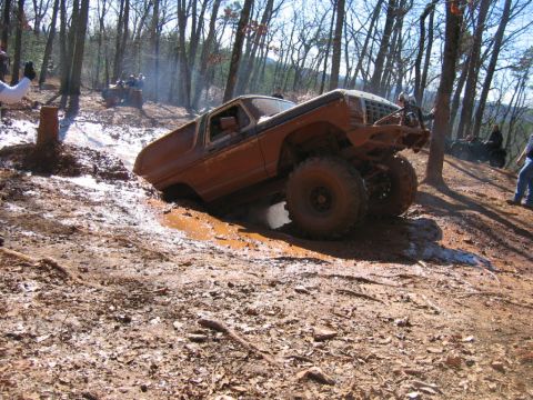 1992 Ford Mustang - An off-road vehicle navigates a challenging muddy terrain with steep inclines and trees in the background.