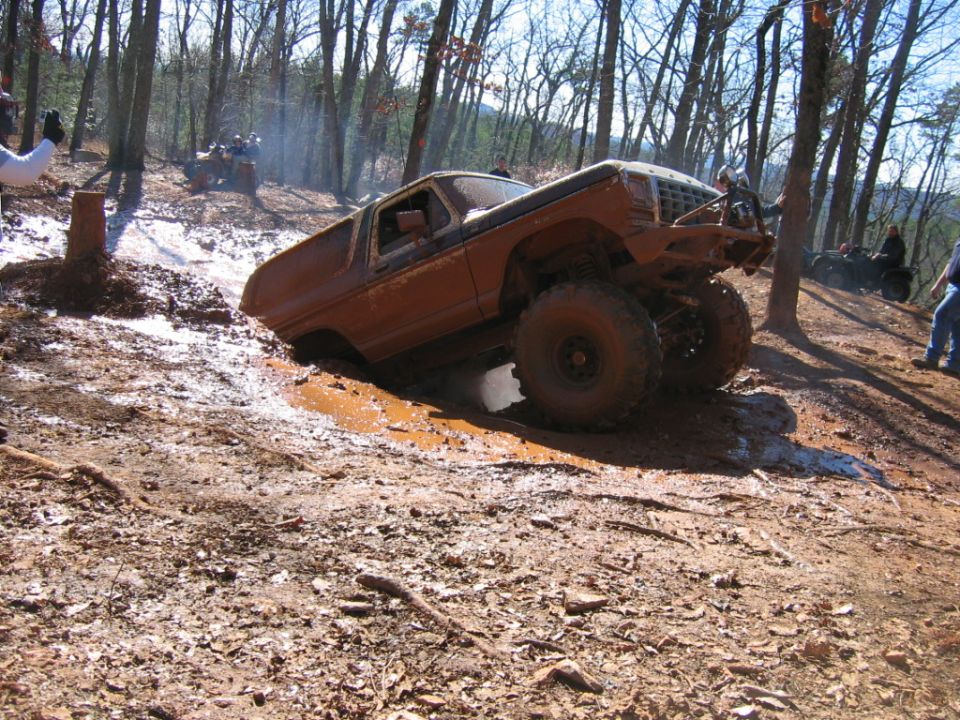 Muddy brown off-road vehicle with large tires stuck in a muddy ditch, front right tire elevated