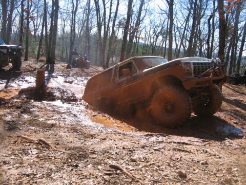 1992 Ford Mustang - An off-road vehicle navigates a muddy trail, with another vehicle visible in the background.