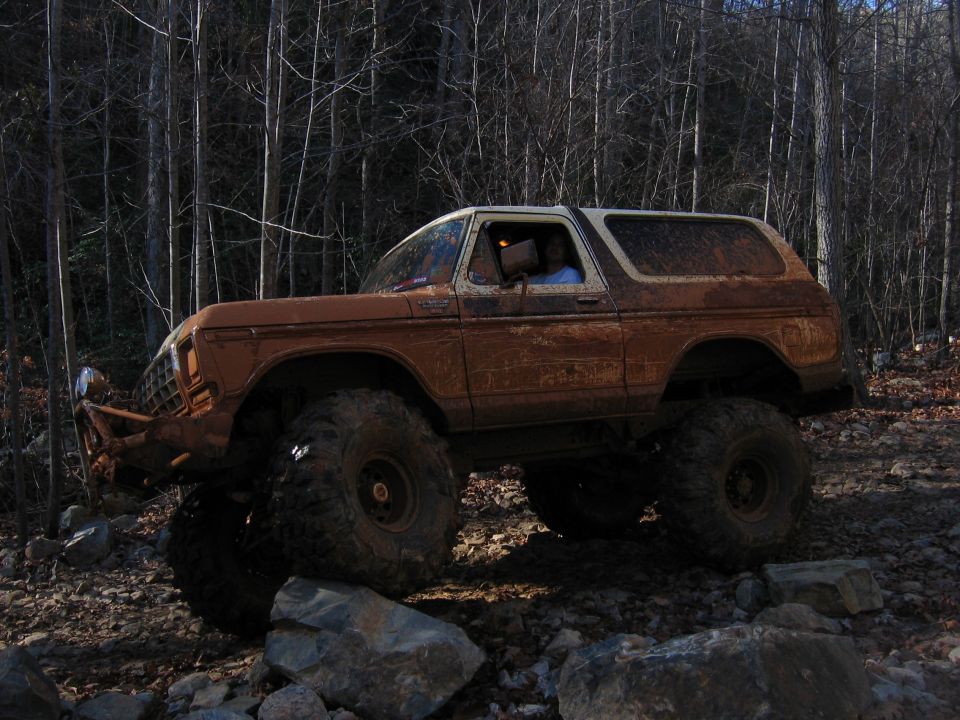 Mud-covered 1978 Ford Bronco with large off-road tires navigating rocky terrain