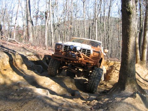1992 Ford Mustang - A heavily modified Ford truck navigates a challenging off-road obstacle course in a wooded area.