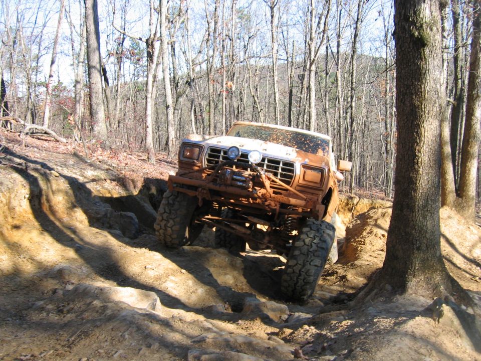 Muddy 1980s Ford F-Series truck climbing over rocks on a wooded trail