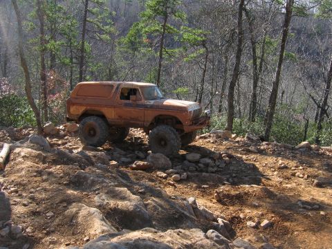 1992 Ford Mustang - Modified 1978 Ford Bronco tackling a challenging rocky trail in a wooded area.