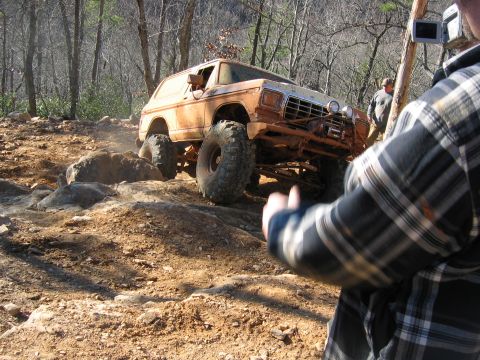 1992 Ford Mustang - A heavily modified off-road vehicle navigates a challenging rocky terrain in a wooded area.