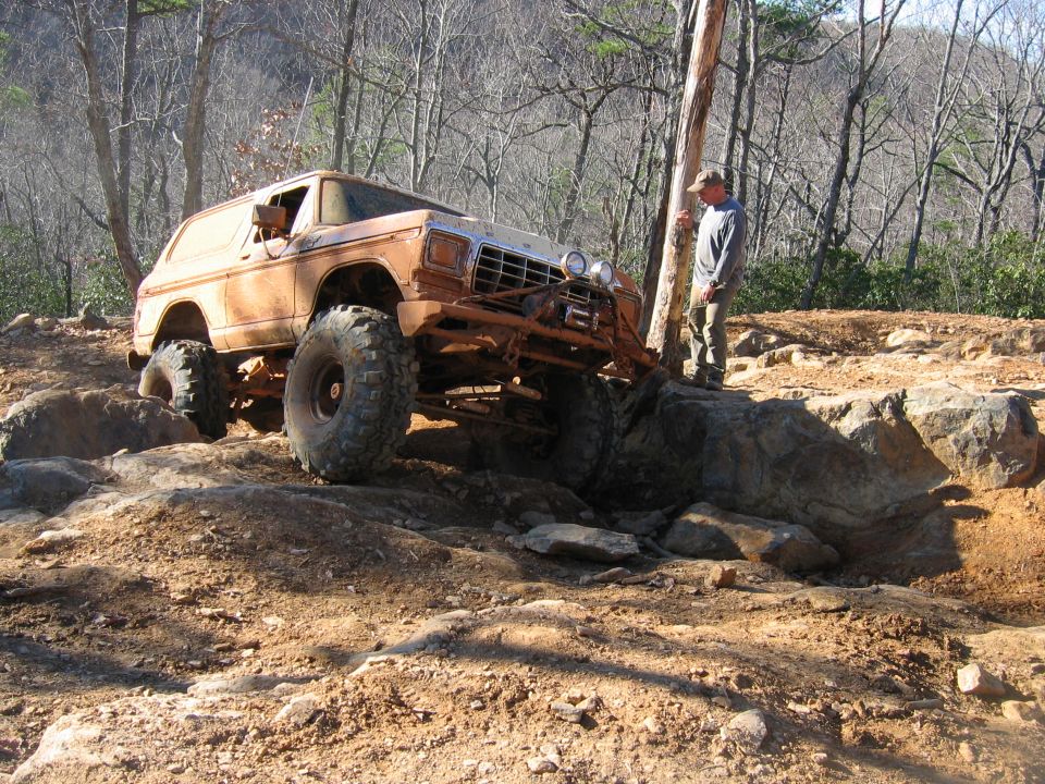Brown off-road SUV with large tires climbing over rocks, front grille visible