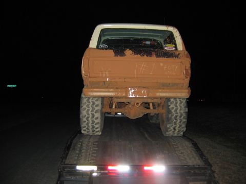 1992 Ford Mustang - A heavily mud-caked pickup truck is loaded onto a trailer at night, with '#1 FOTY' visible on its tailgate.