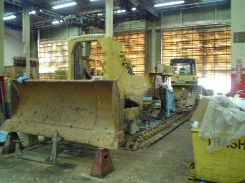 1966 International School Bus - A yellow bulldozer with a large blade is supported by stands in a workshop, with another bulldozer visible in the background.