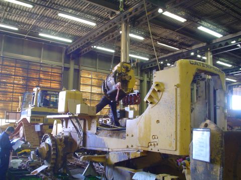 1966 International School Bus - Mechanics work on heavy machinery inside a large industrial building.