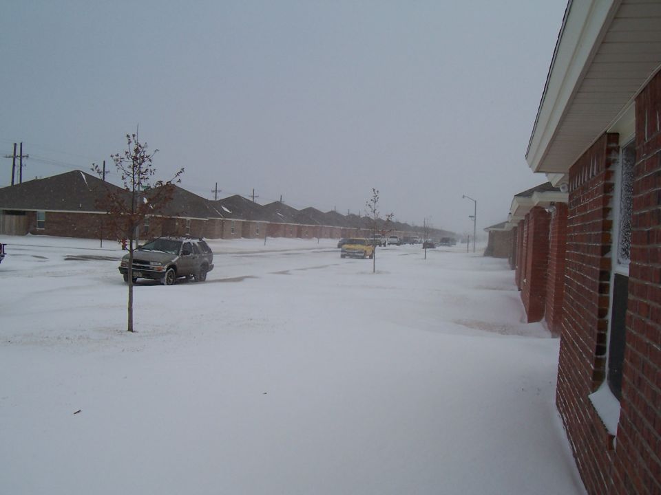 Silver SUV parked on a snow-covered street with houses in the background