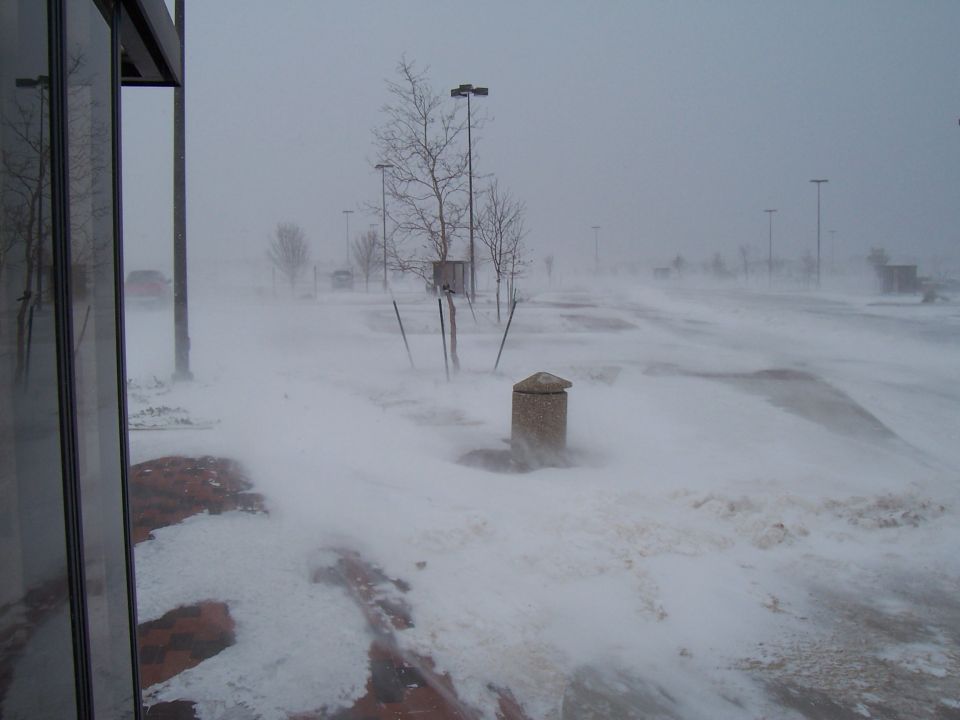 Parking lot obscured by blowing snow, with a red car visible in the distance