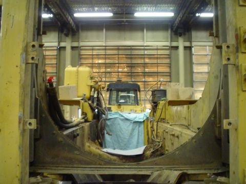 1966 International School Bus - A yellow bulldozer is parked inside a workshop, partially covered with a blue tarp, with large metal structures surrounding it.