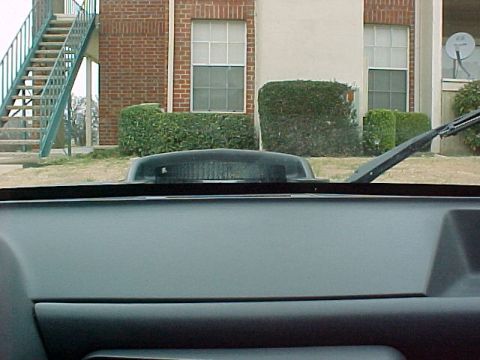 1990 Ford Bronco - A black hood scoop with a ribbed texture is visible through the windshield, with a building and stairs in the background.