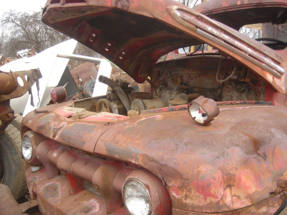 Rusty red truck engine bay with hood open. Headlights and grille visible