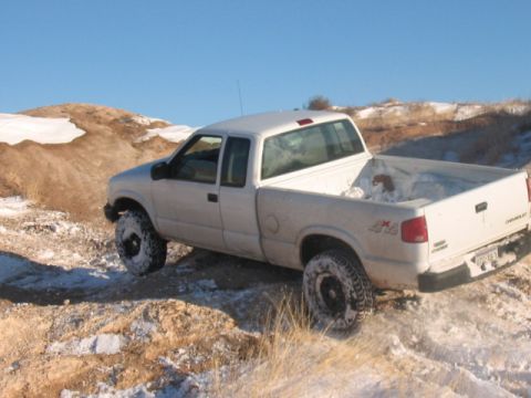 2003 Ford Ranger - A white pickup truck navigates a snowy, off-road terrain under a clear blue sky.