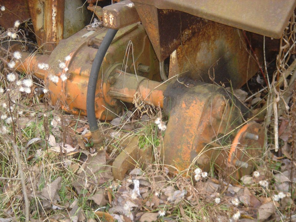 Rusty orange differential and axle components in overgrown grass