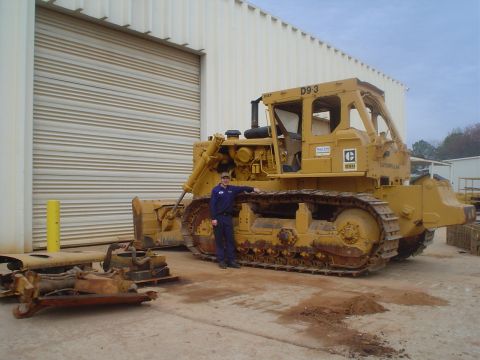 1966 International School Bus - A Caterpillar D9-3 bulldozer is shown with a person standing next to it in front of a large garage door.