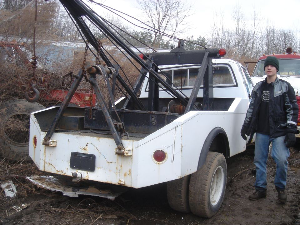 White tow truck with a black crane, rear view. Rusty body, dual rear wheels