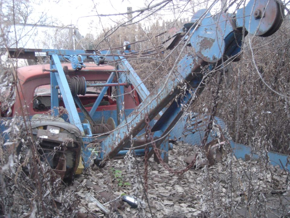 Tow truck with red cab and blue boom, overgrown with weeds