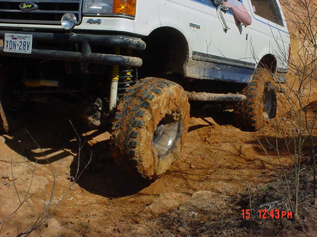 Close-up of front tire drooping off a white Ford 4x4 over a red-clay ledge, Texas plate XDN-28V
