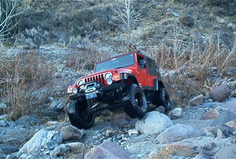 1986 Ford Bronco - This red Jeep Wrangler is shown off-roading on a rocky, uneven surface.