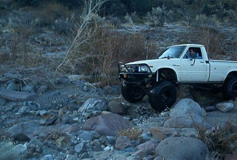 1986 Ford Bronco - Modified pickup truck navigates rocky terrain in an off-road setting.
