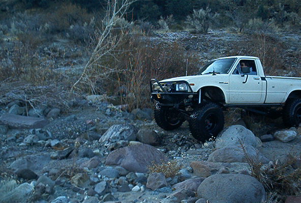 White pickup truck with off-road modifications driving over rocks