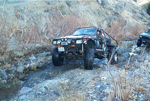 1986 Ford Bronco - This heavily modified off-road vehicle navigates a challenging rocky trail, with another vehicle visible in the background.