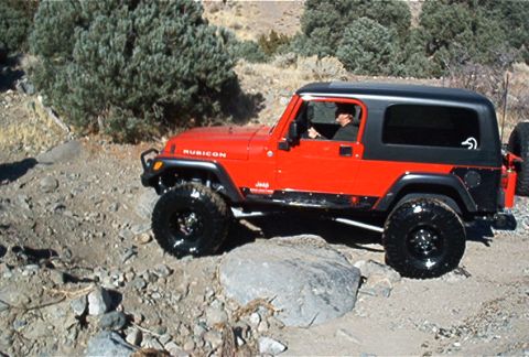 1986 Ford Bronco - A red Jeep Wrangler Rubicon navigates a rocky off-road path.