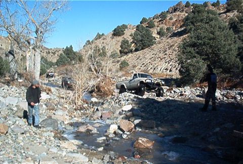 1986 Ford Bronco - A pickup truck navigates a rocky stream bed in a mountainous area.