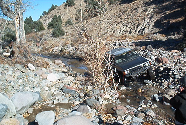 Black SUV navigating a rocky stream bed, off-roading