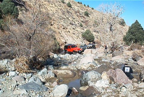 1986 Ford Bronco - Off-road vehicles navigate a challenging rocky stream bed in a desert landscape.