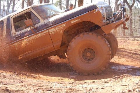 1992 Ford Mustang - A heavily mud-covered truck with oversized tires navigates a muddy terrain, kicking up dirt and water.