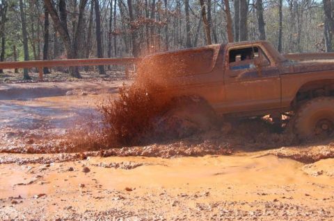 1992 Ford Mustang - An off-road vehicle navigates a challenging muddy terrain, kicking up a large spray of mud.