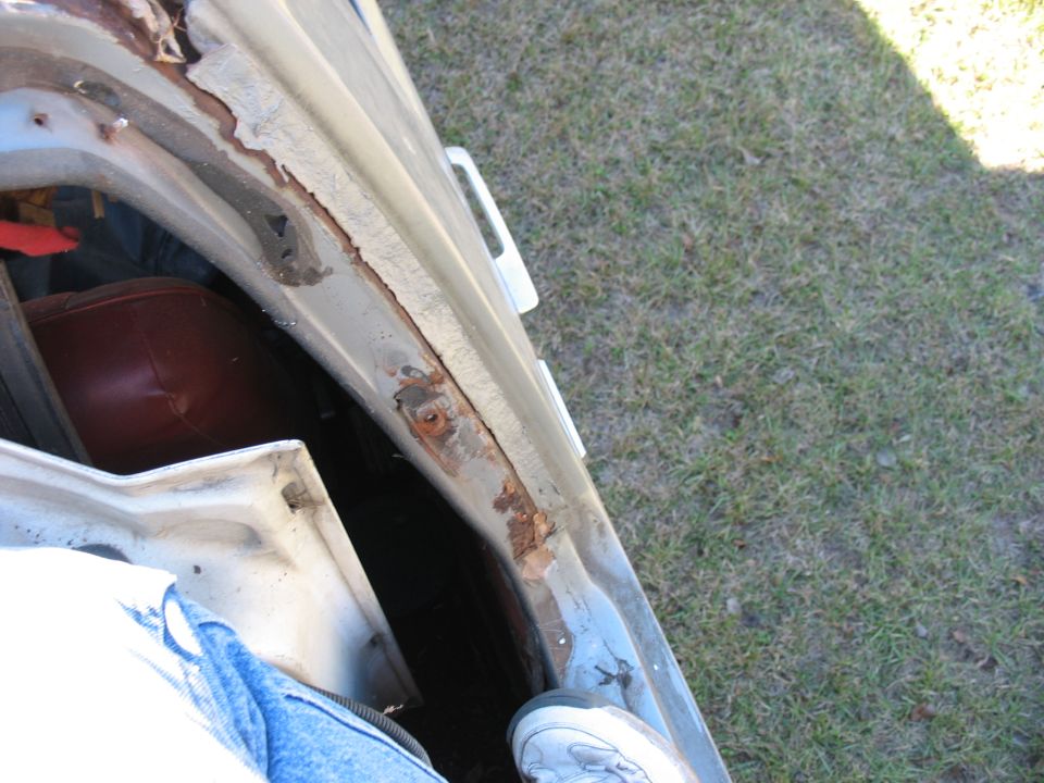 Rusted drip rail and pillar seam in open white truck door opening, red interior panel visible