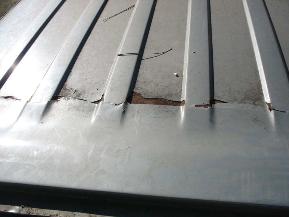Torn and rusting seam across a ribbed silver truck roof panel, jagged edges and loose wires