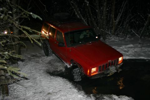 2003 Jeep TJ - A red Jeep Cherokee XJ navigates a snowy, watery path in the dark.