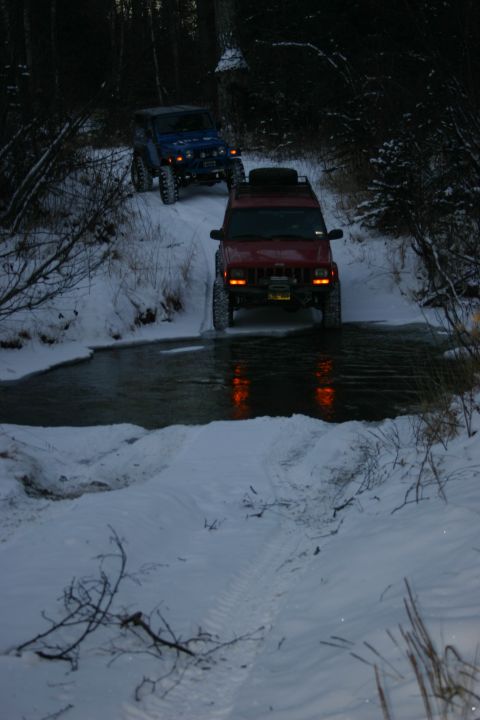 2003 Jeep TJ - Two Jeeps navigate a snowy trail and creek crossing in a wooded area.
