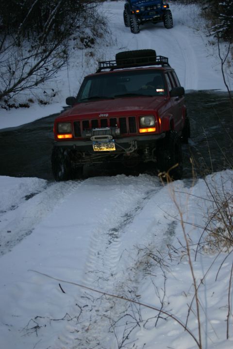 2003 Jeep TJ - A red Jeep Cherokee XJ navigates a snowy path, followed by a blue Jeep Wrangler.