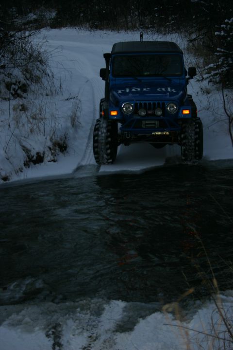 2003 Jeep TJ - A blue Jeep navigates a winter stream on a snowy trail.