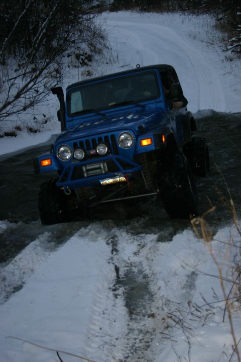 2003 Jeep TJ - A blue 2003 Jeep Wrangler navigates a snowy, watery path in a wooded area.