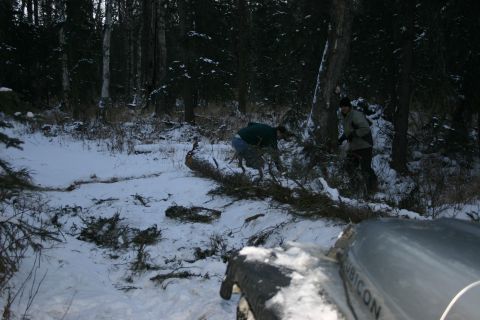 2003 Jeep TJ - Silver Jeep Wrangler Rubicon parked in a snowy forest scene with two people near a fallen tree.