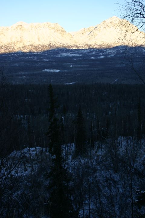 2003 Jeep TJ - Sunlight hits the peaks of snow-covered mountains above a dark, wooded valley.