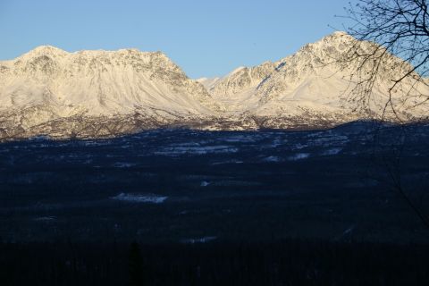 2003 Jeep TJ - A vast mountain range, dusted with snow, looms over a shadowed forest landscape under a bright sky.
