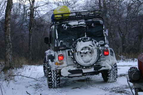 2003 Jeep TJ - A white Jeep Wrangler is seen from the rear, covered in snow, with a yellow cargo bag on its roof rack.