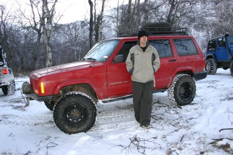 2003 Jeep TJ - Man standing next to a red Jeep Cherokee XJ in a snowy wooded area with another Jeep in the background.