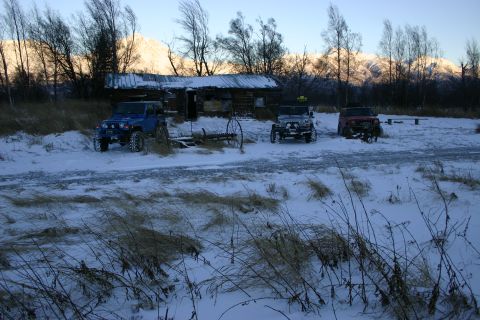 2003 Jeep TJ - Three Jeep Wranglers are parked in the snow in front of a rustic log cabin with mountains in the background.